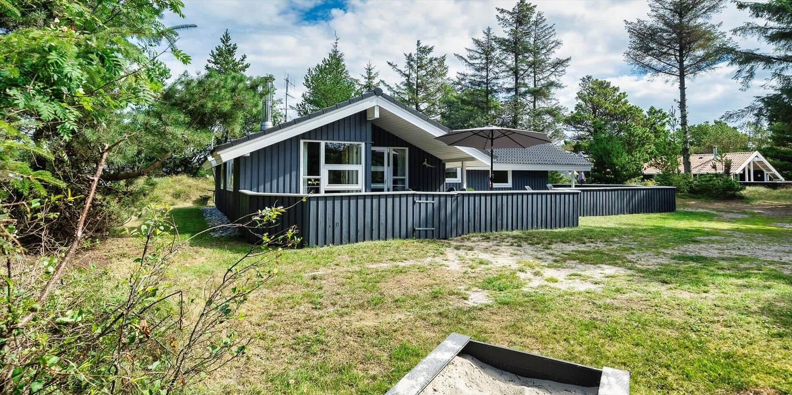 Ein dunkelblaues Ferienhaus mit Garten und Sonnenschirm inmitten von Bäumen.