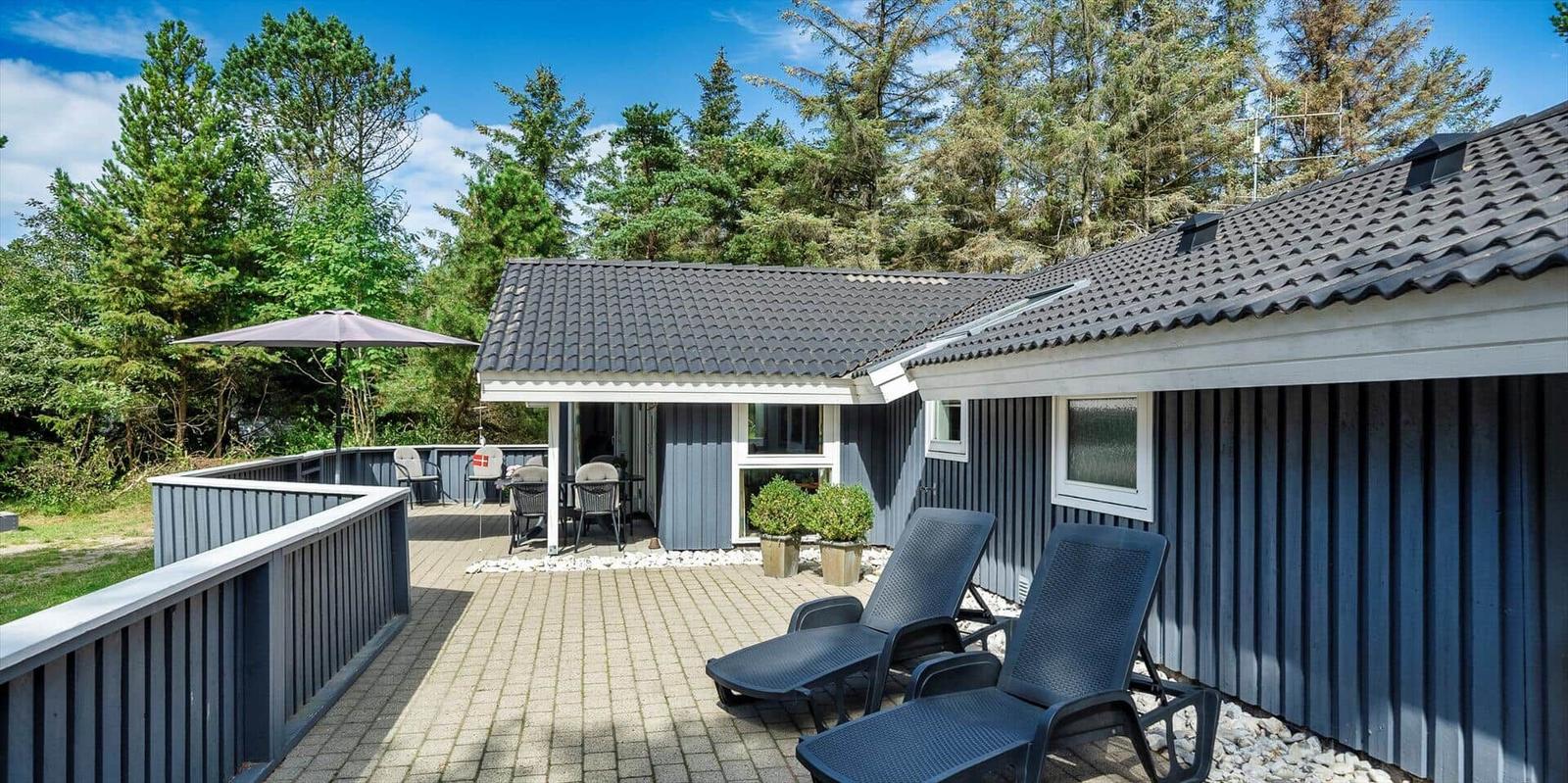 Terrasse mit Liegestühlen und Sonnenschirm vor einem blauen Haus mit Dach