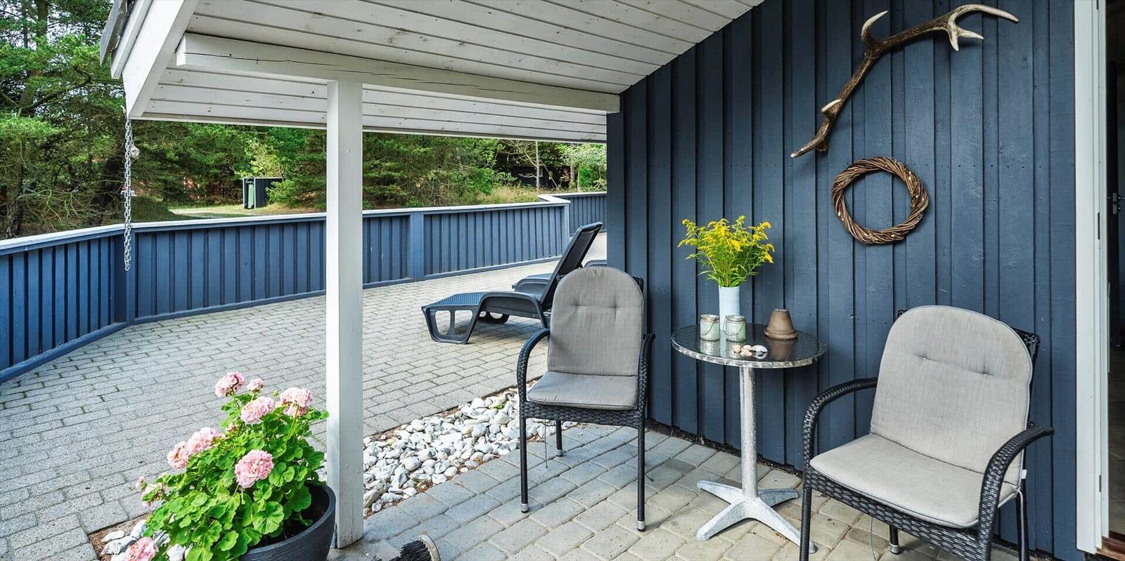 Terrasse mit zwei Stühlen, Tisch und Liegestuhl. Wand mit Hirschgeweih und Kranz.