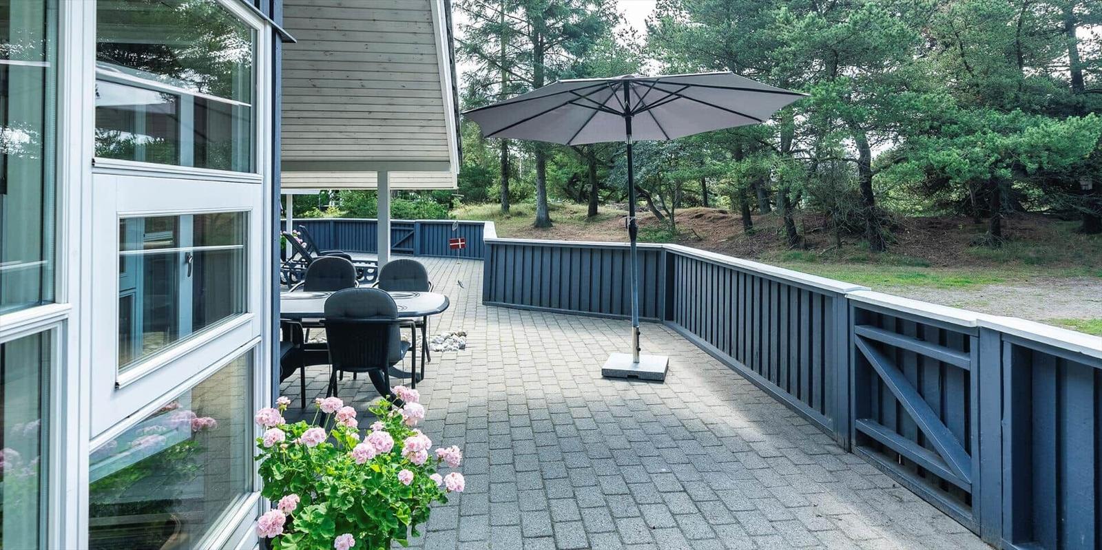 Terrasse mit Tisch, Stühlen und Sonnenschirm. Umgeben von Bäumen und einem Zaun.