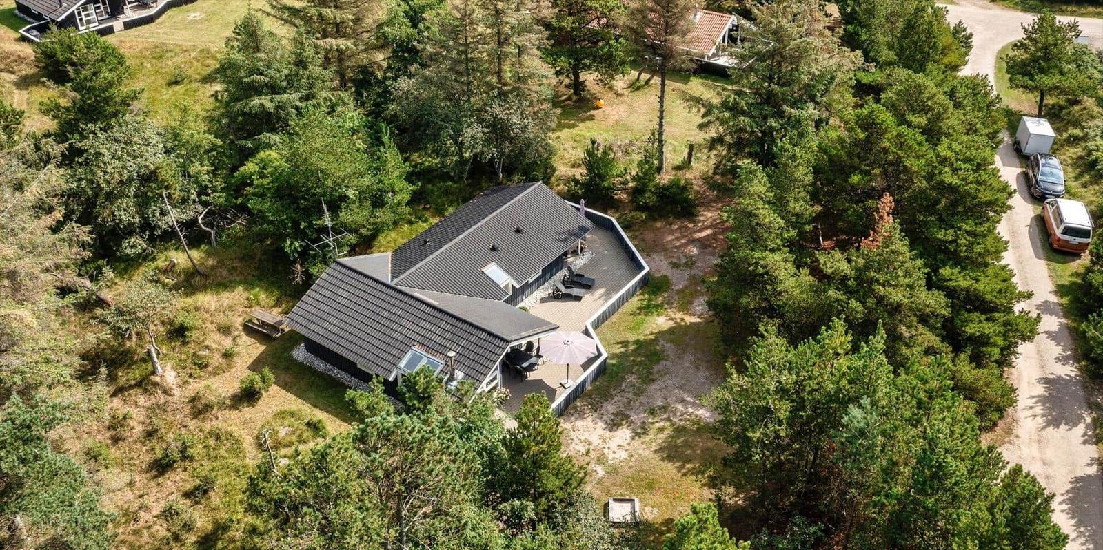 Haus mit Terrasse und Grillplatz im Wald. Parkplatz mit Fahrzeugen.