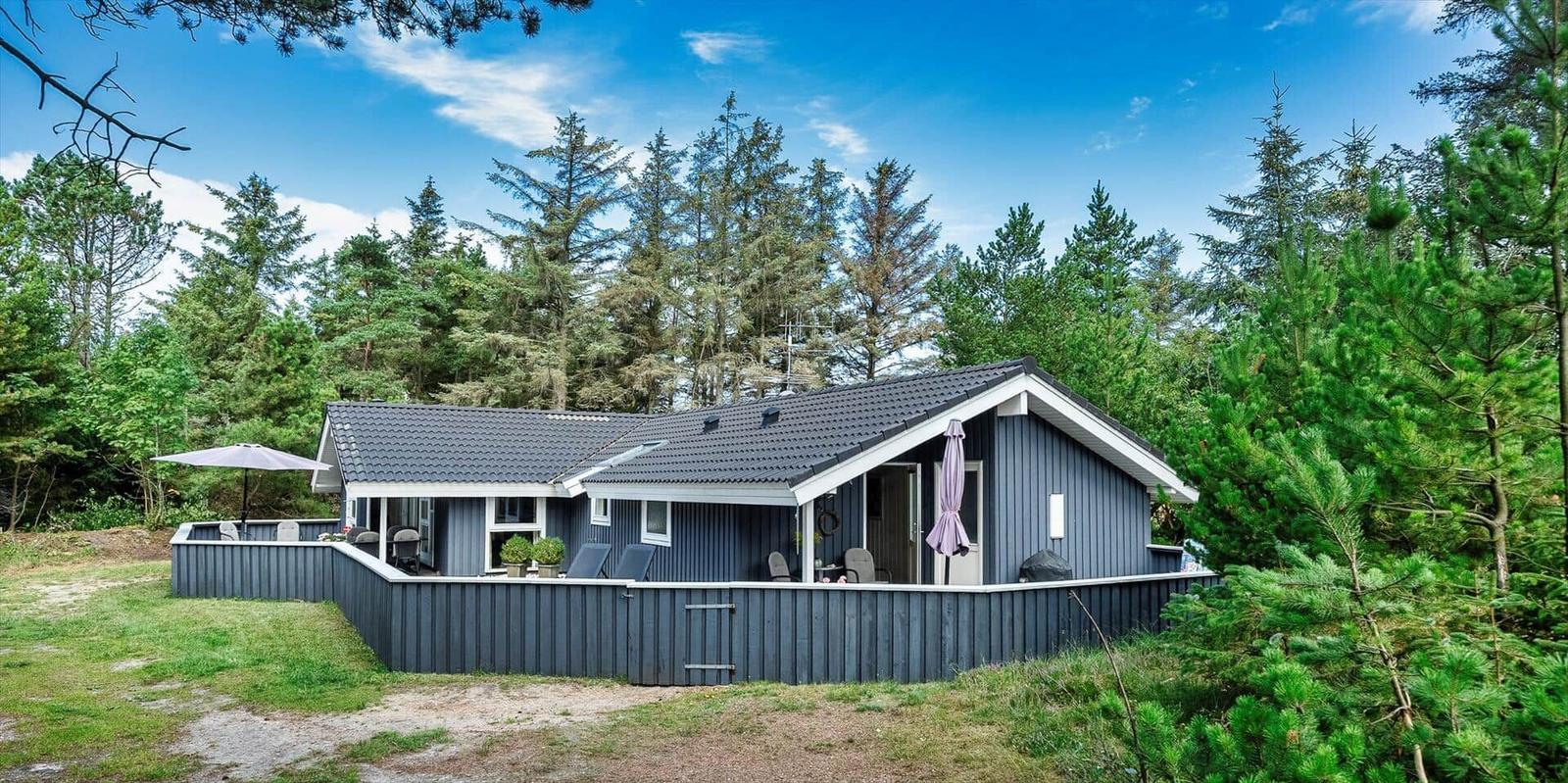 Ein graues Ferienhaus mit Terrasse und Grillplatz im Wald.