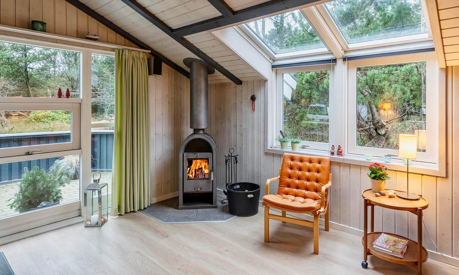 Raum mit Kamin, brauner Ledersessel und großen Fenstern mit Blick auf Grün.