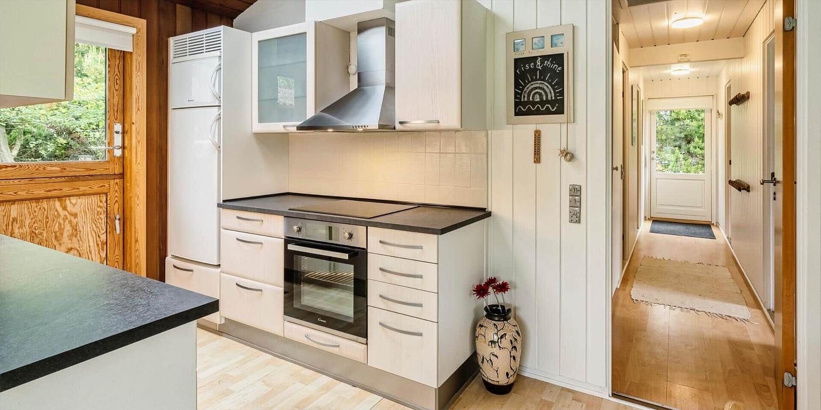 Küche mit Dunstabzug, Kühlschrank und Ofen. Flur mit Holzboden und Tür.