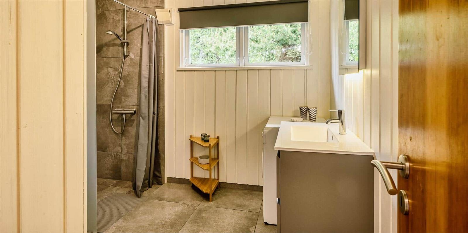 Badezimmer mit Dusche, Waschbecken und Fenster mit Blick auf Bäume.