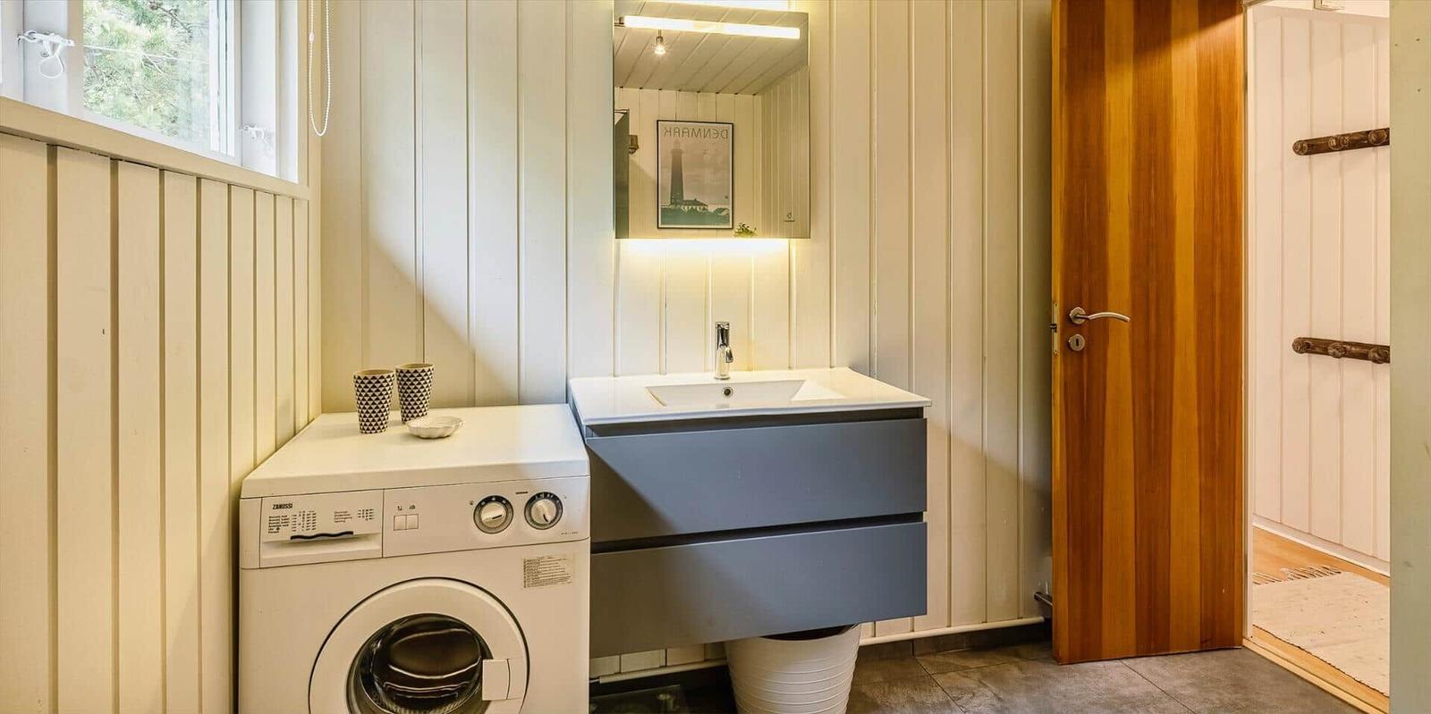 Badezimmer mit Waschmaschine, Spiegel und Holztür.
