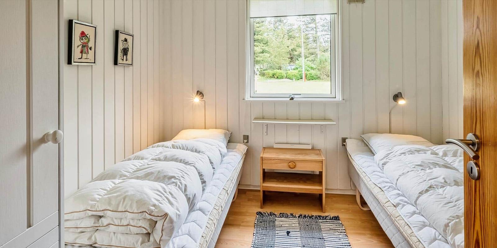 Zwei Betten mit weißen Bettwäsche, Holzkommode und Fenster mit Blick auf Grünflächen.