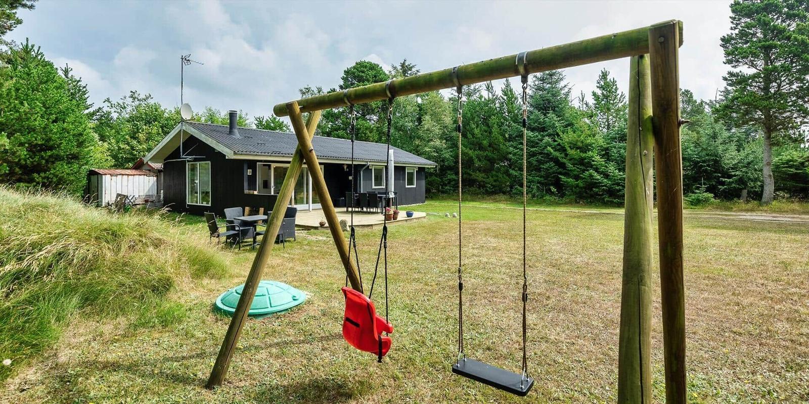 Schwarzes Haus mit Spielplatz und Garten. Roter Sitzschwinger und Holzschaukel.