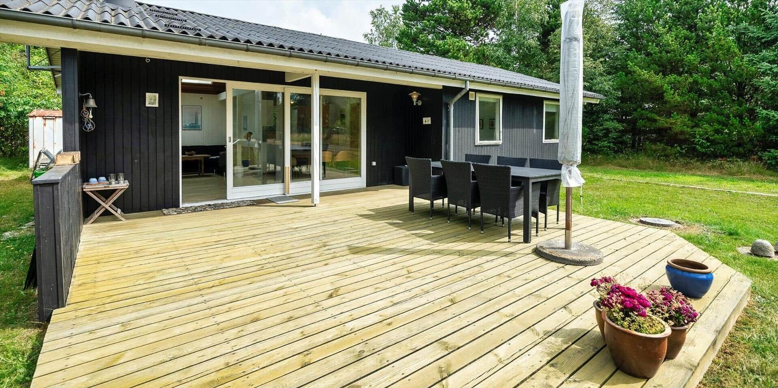Holzterrasse mit Sitzgruppe und Blick ins Haus. Garten mit Pflanzen und Bäumen.