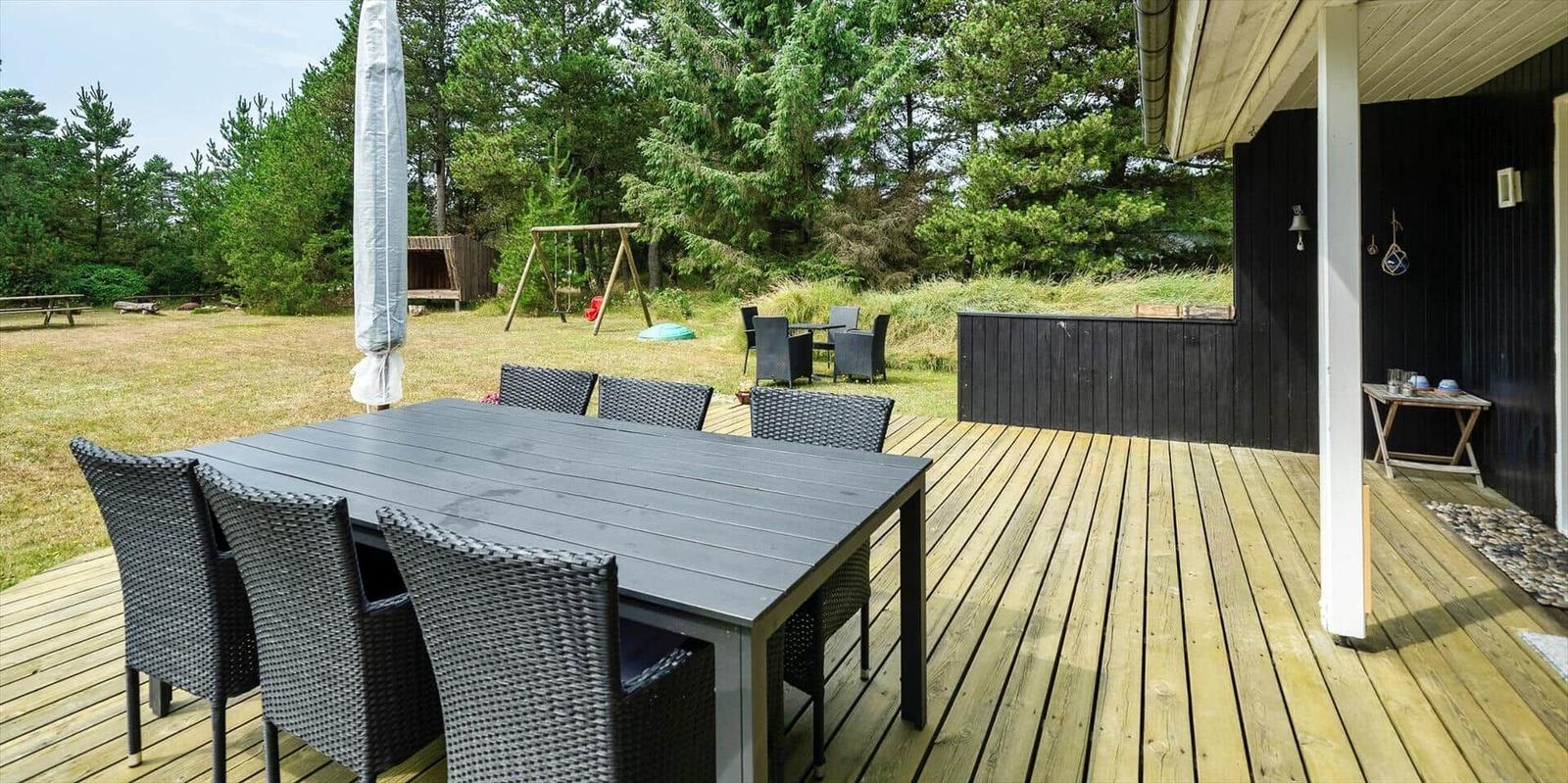 Terrasse mit Tisch und Stühlen, Blick auf Grasfläche und Spielplatz.