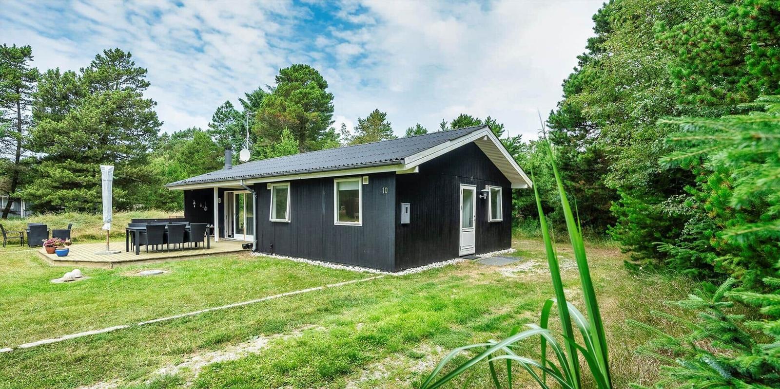 Schwarzes Ferienhaus mit Terrasse, Garten und umgeben von Bäumen.