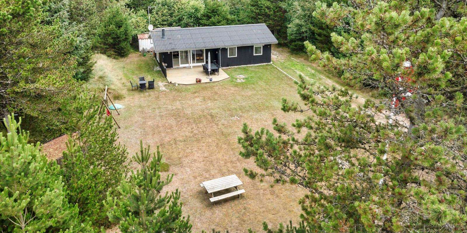 Ein Haus mit Terrasse, Garten und Picknicktisch umgeben von Bäumen.