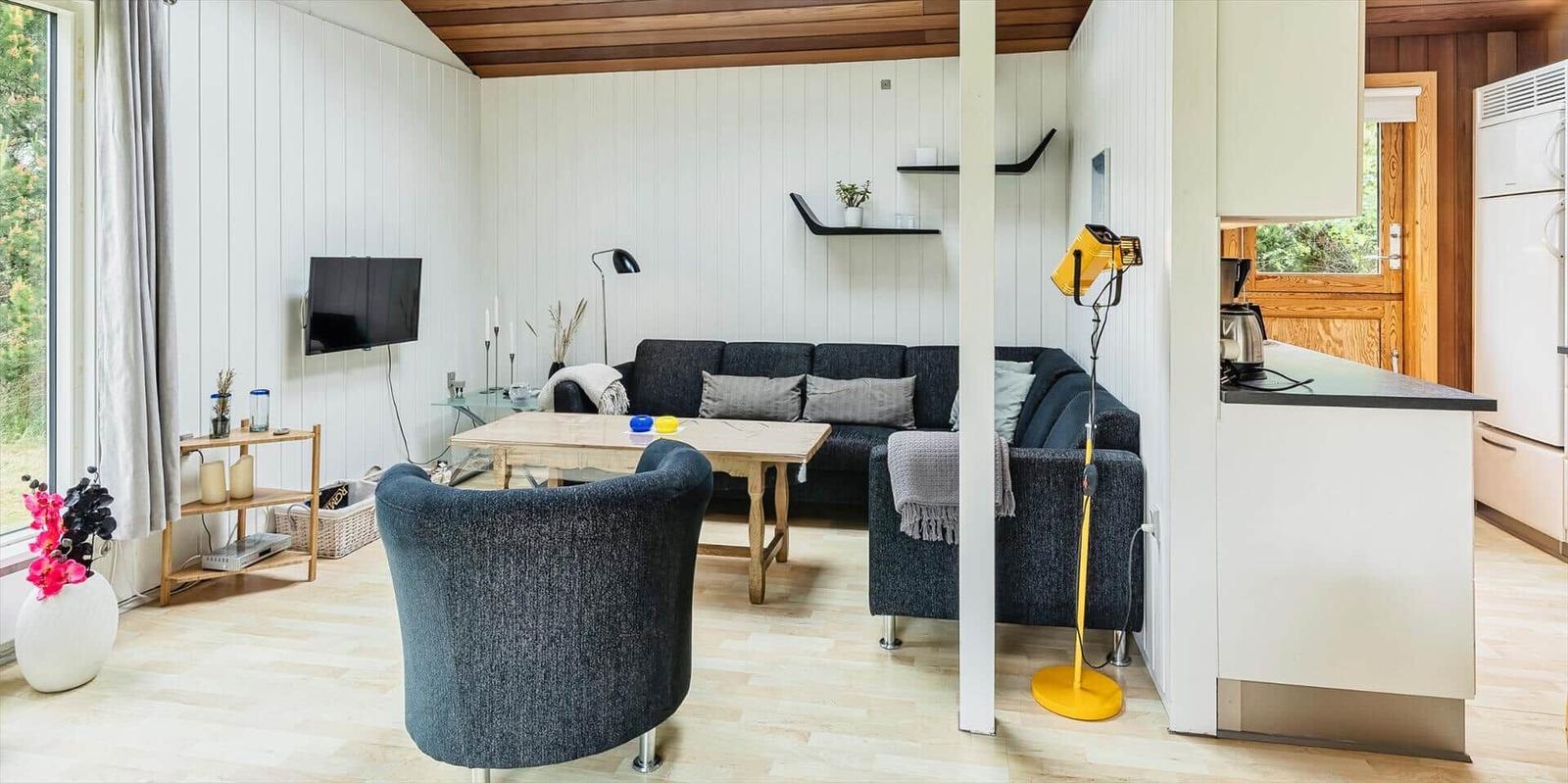 Wohnbereich mit Sofa, Tisch und Fernseher. Küche mit Arbeitsplatte und Kühlschrank.