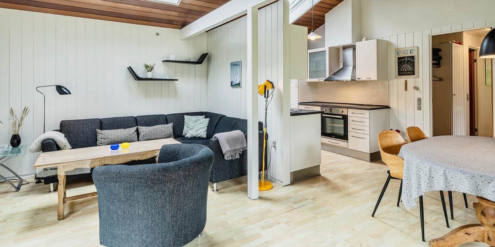Wohnbereich mit Sofa, Esstisch und Küche. Holzfußboden und weiße Wände.