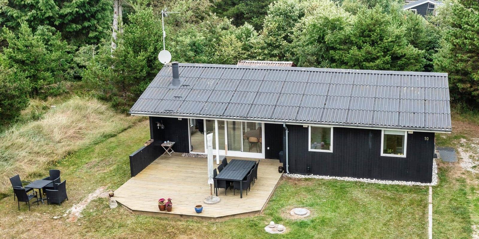Schwarzes Ferienhaus mit Holzterrasse, Garten und Satellitenschüssel.