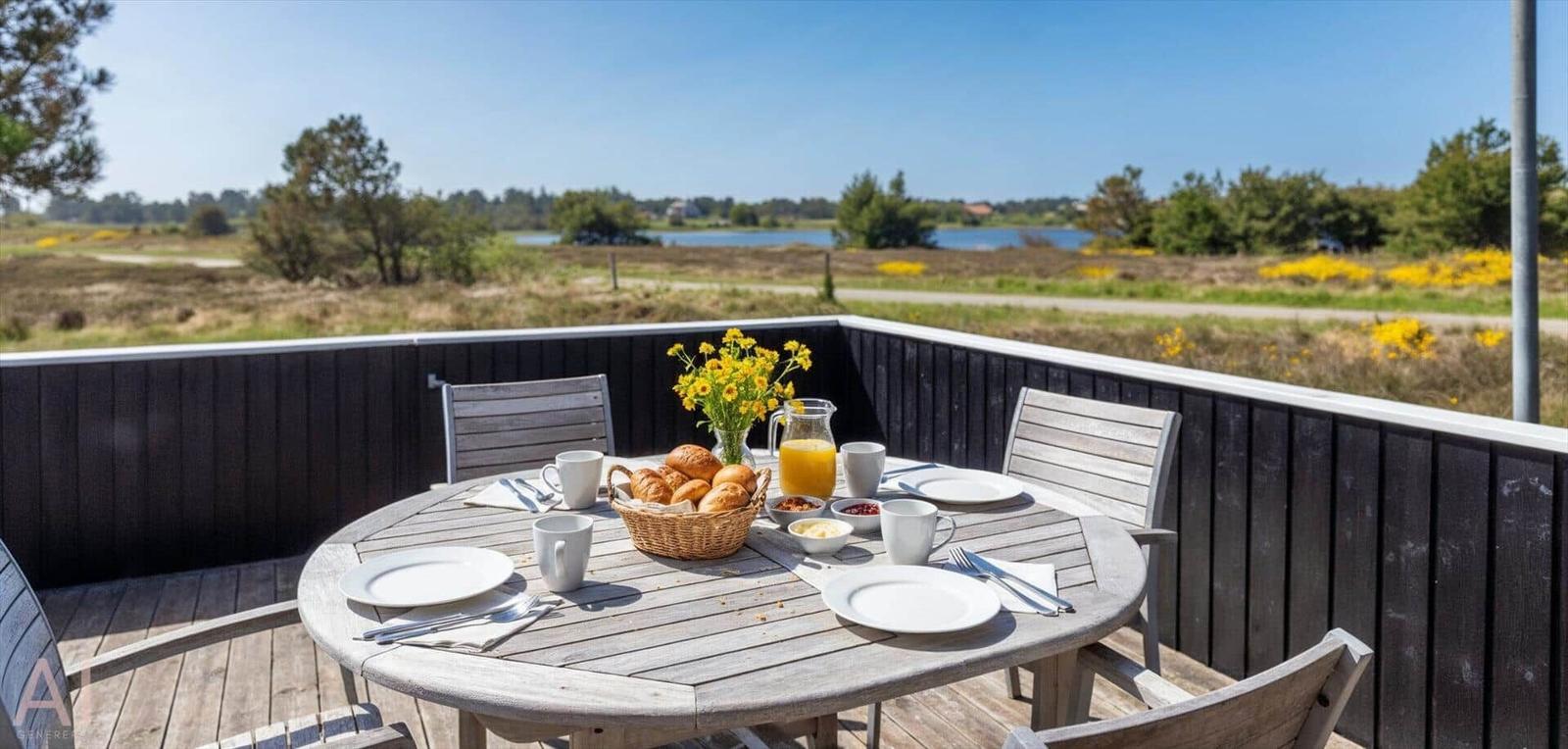 Rundtisch mit Frühstück auf Terrasse mit Blick auf Wasser und Wiesen.