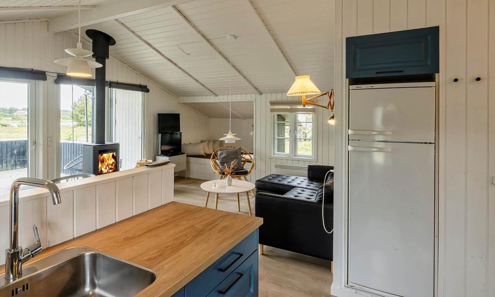 Küche mit Holzplatte und Kühlschrank. Wohnbereich mit Sofa, Kamin und TV.