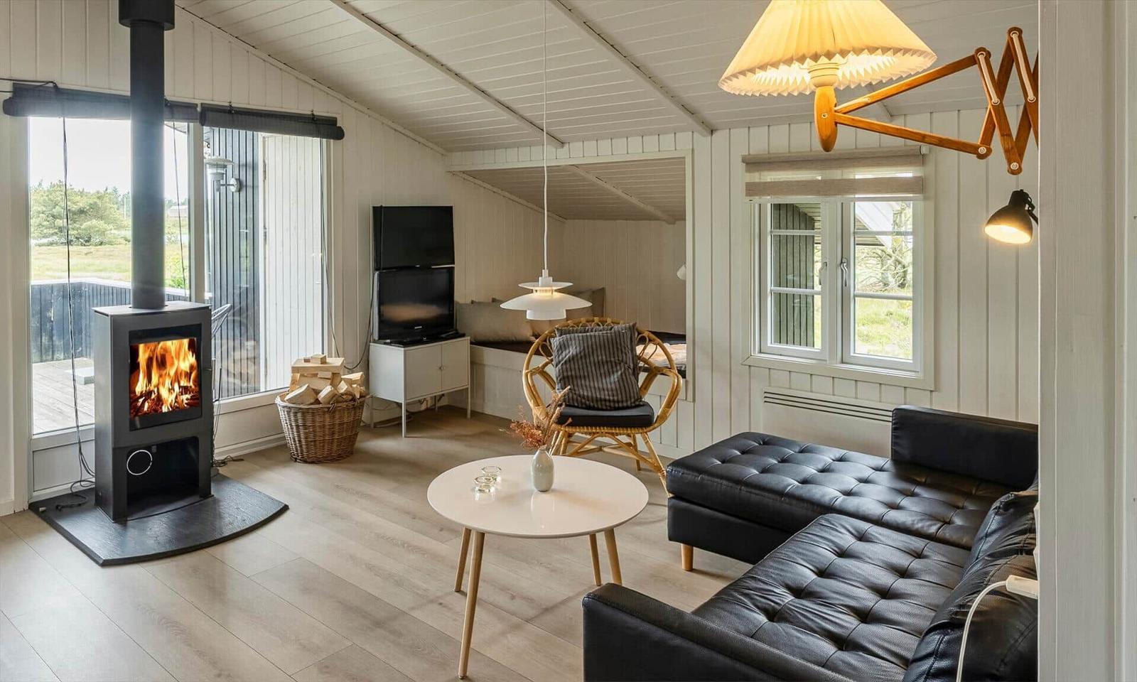 Wohnzimmer mit Kamin, Sofa und Fernseher. Holzdielen und große Fenster.