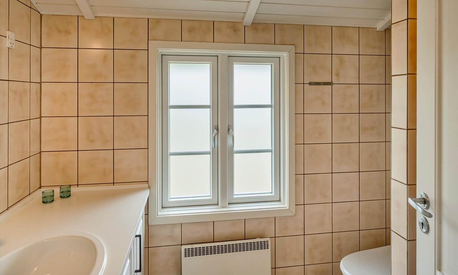 Bad mit Fliesenwand, Fenster und Waschtisch.
