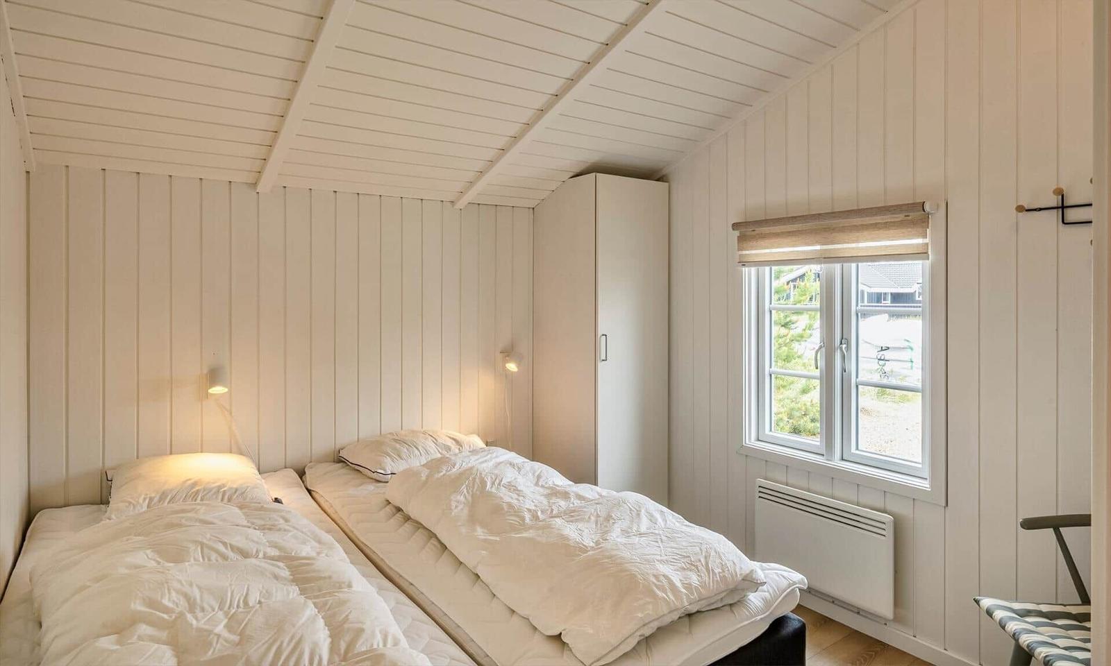 Zwei Betten mit weißen Bettwäschen, weißer Holzwand und Fenster mit Blick nach draußen.