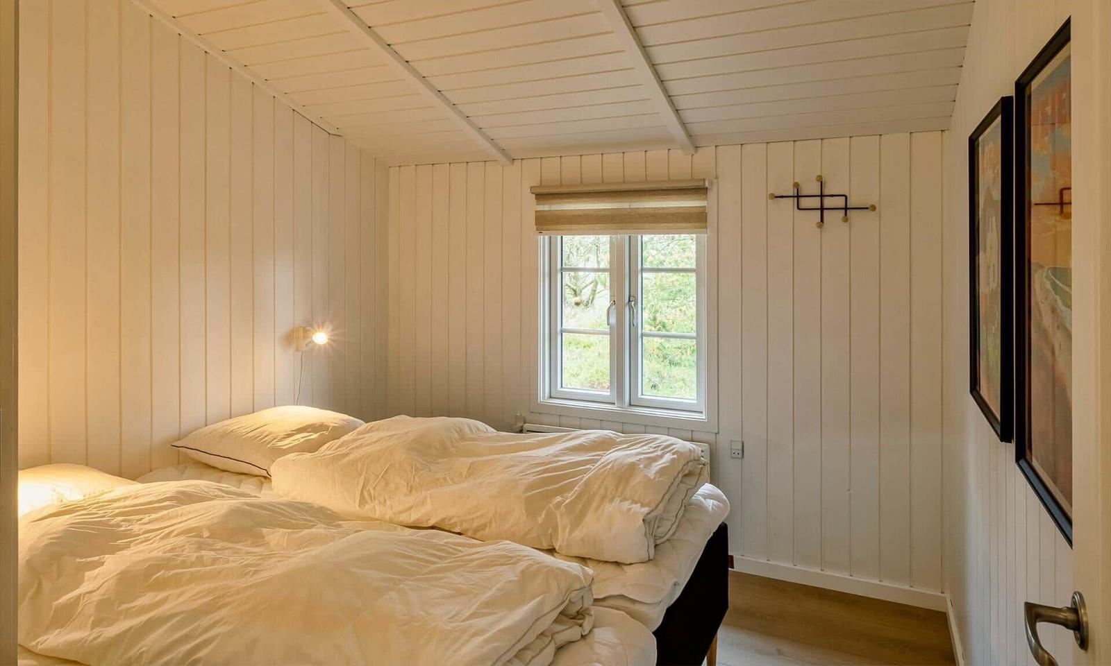 Schlafzimmer mit Doppelbett, Fenster und Holzwandverkleidung.