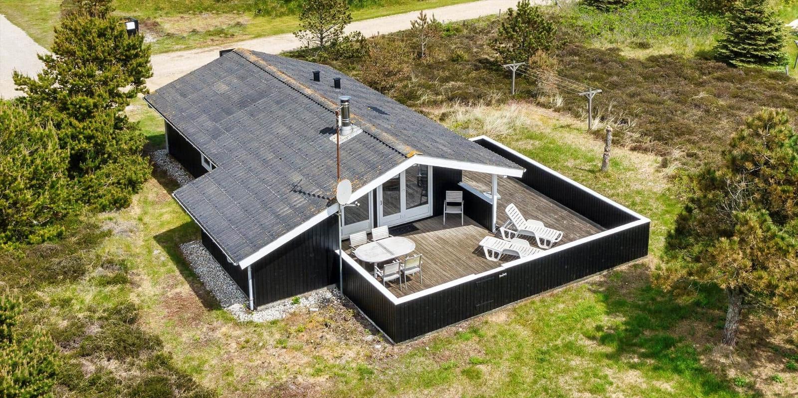 Schwarzes Haus mit Terrasse, Tisch, Stühlen und Liegestühlen im Grünen.