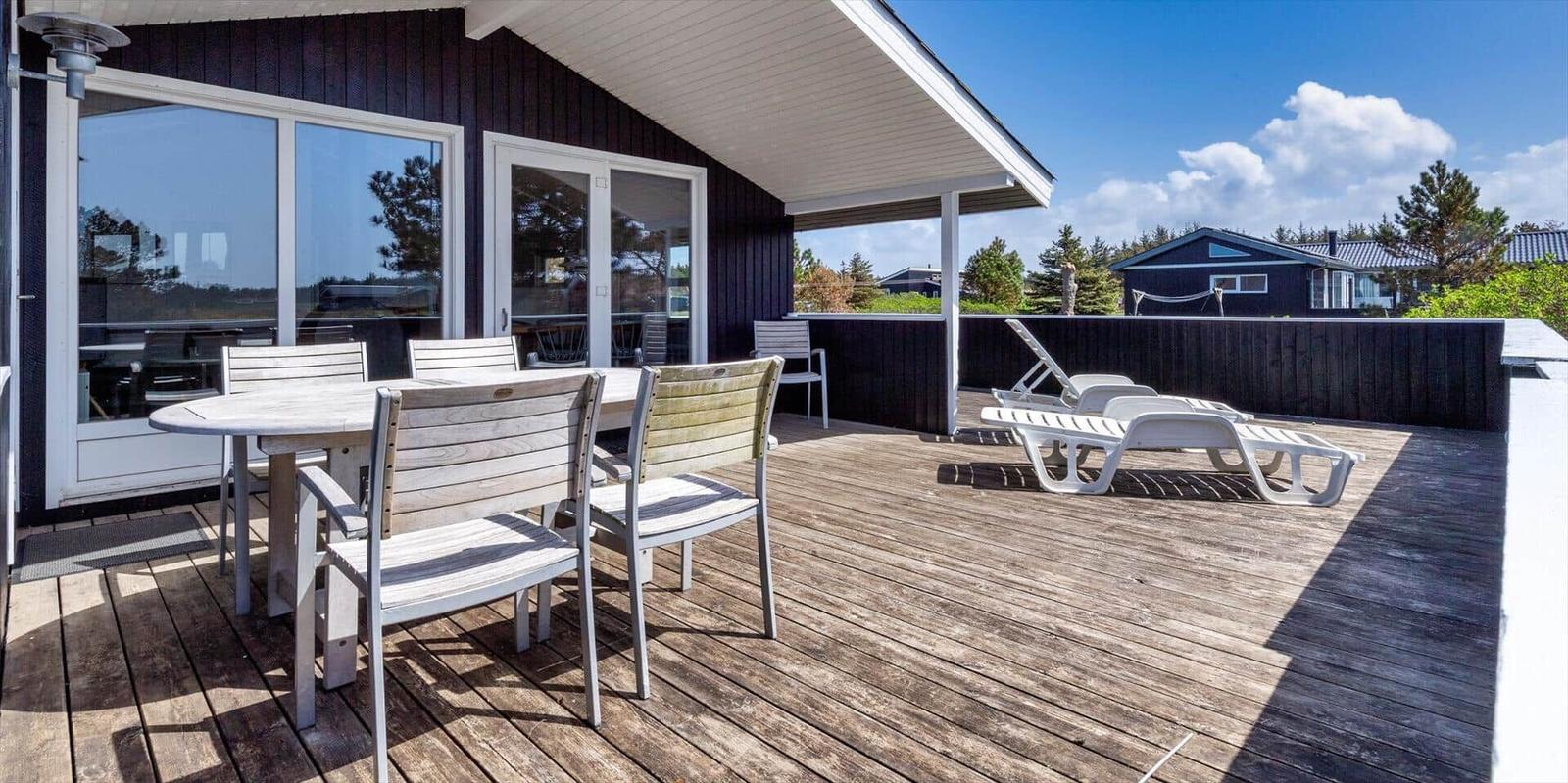 Terrasse mit Tisch, Stühlen und Liegen. Dunkle Holzwände und weißer Balkon.