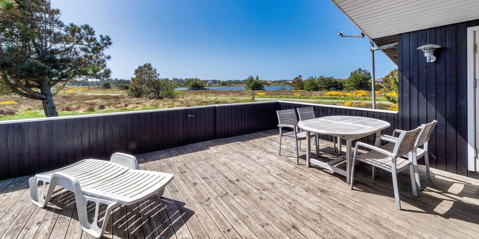 Terrasse mit Tisch, Stühlen und Liegestuhl. Blick auf Grünland und Wasser.