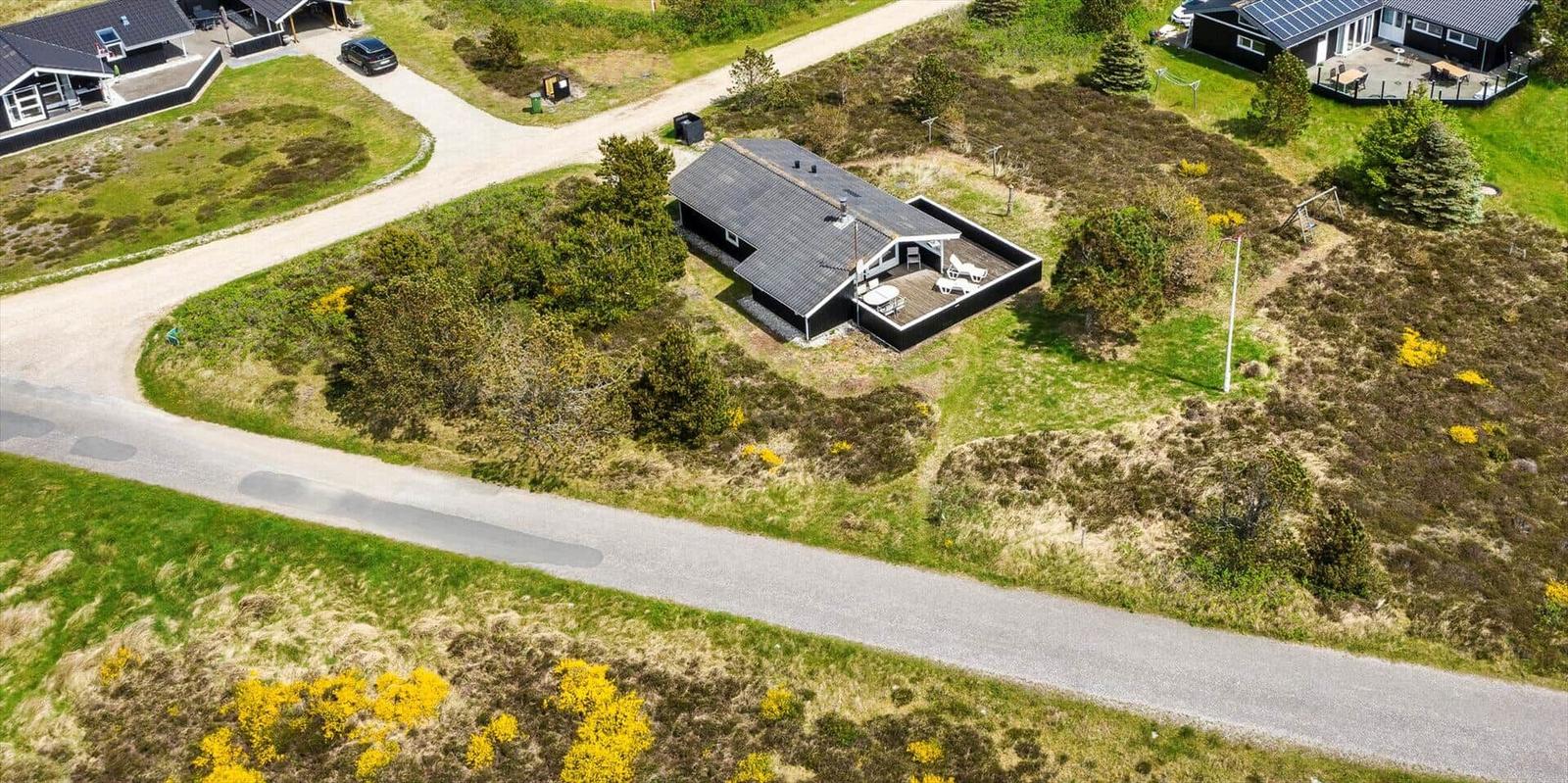 Haus mit Terrasse und Garten, umgeben von Gras und Bäumen.
