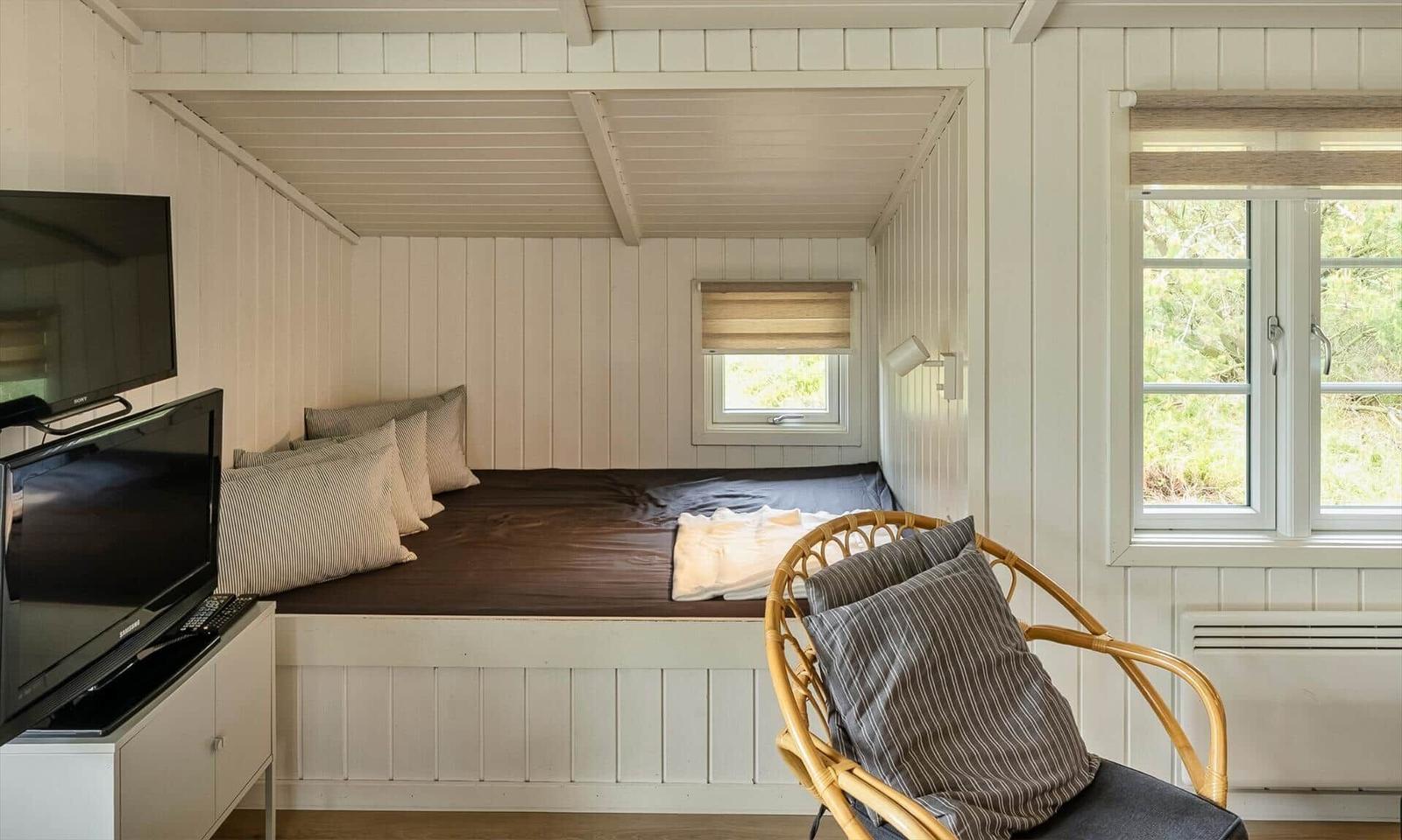Schlafzimmer mit Bett, Stuhl und Fenster. Wandverkleidung und TV sichtbar.