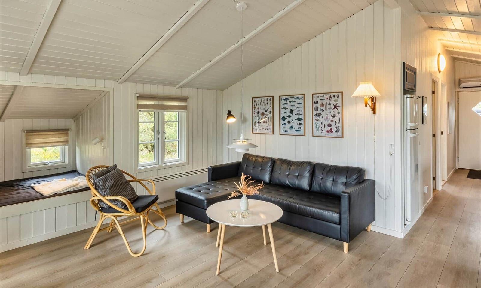 Wohnzimmer mit Sofa, Stuhl und Küchenbereich. Holzdielen und weiße Wände.