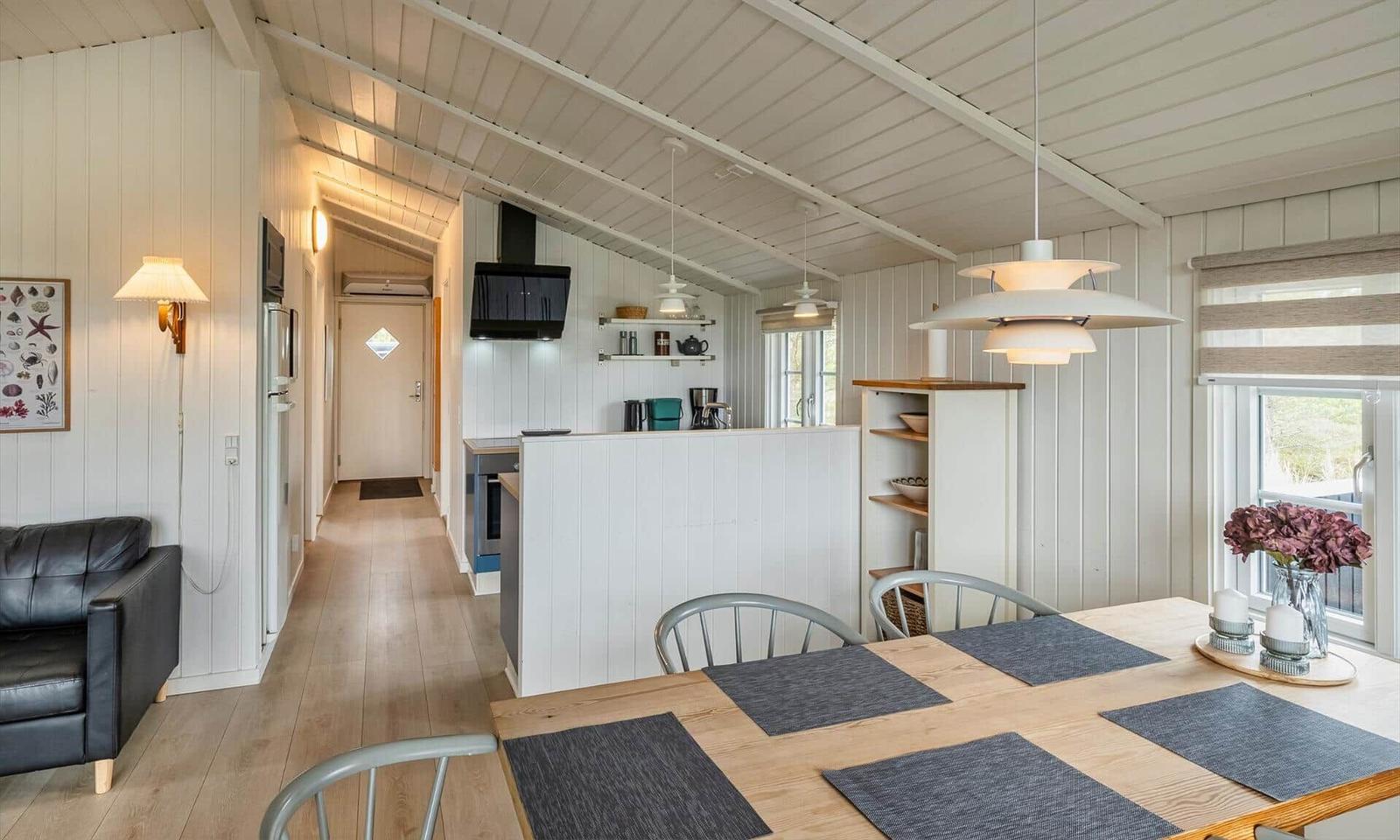 Küche und Essbereich mit Tisch, Stühlen und Fenster. Wohnbereich mit Sofa und Wandbehang.
