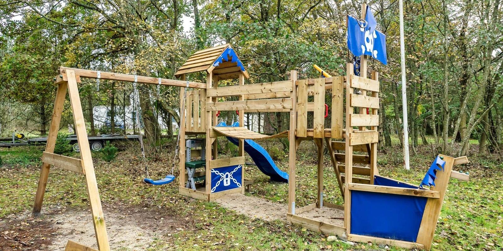 Holzspielplatz mit Schaukel, Rutsche und Piratenschiff im Wald.