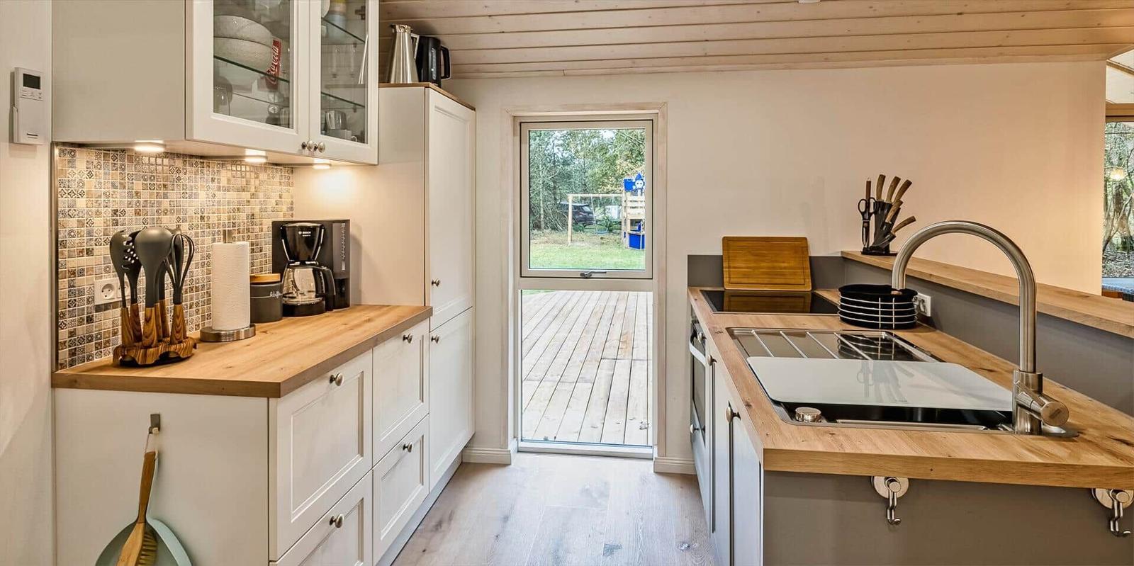 Küche mit Holz Arbeitsplatten, Fenster zur Terrasse und moderner Spüle.