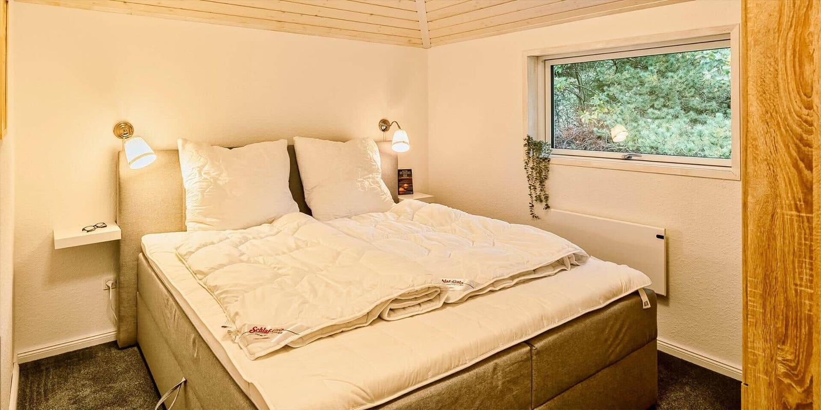Schlafzimmer mit Doppelbett, Fenster und Wandlampen.