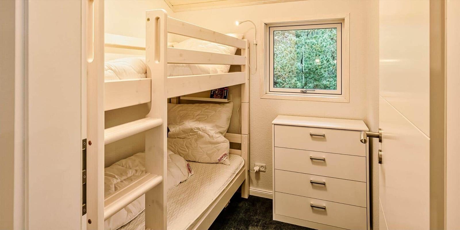 Zimmer mit Doppelstockbett, Schrank und Fenster mit Blick auf Bäume.