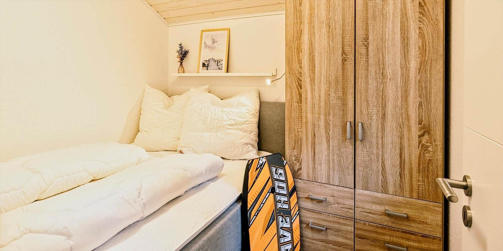 Schlafzimmer mit Bett, Kleiderschrank und Wandregal mit Bild und Pflanze.