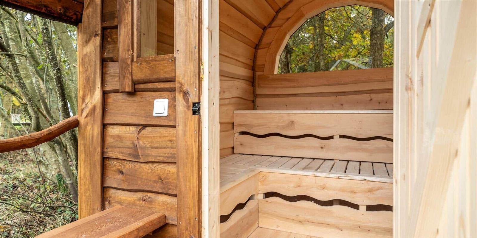Holzsauna mit Sitzbänken und Bogenfenster im Wald