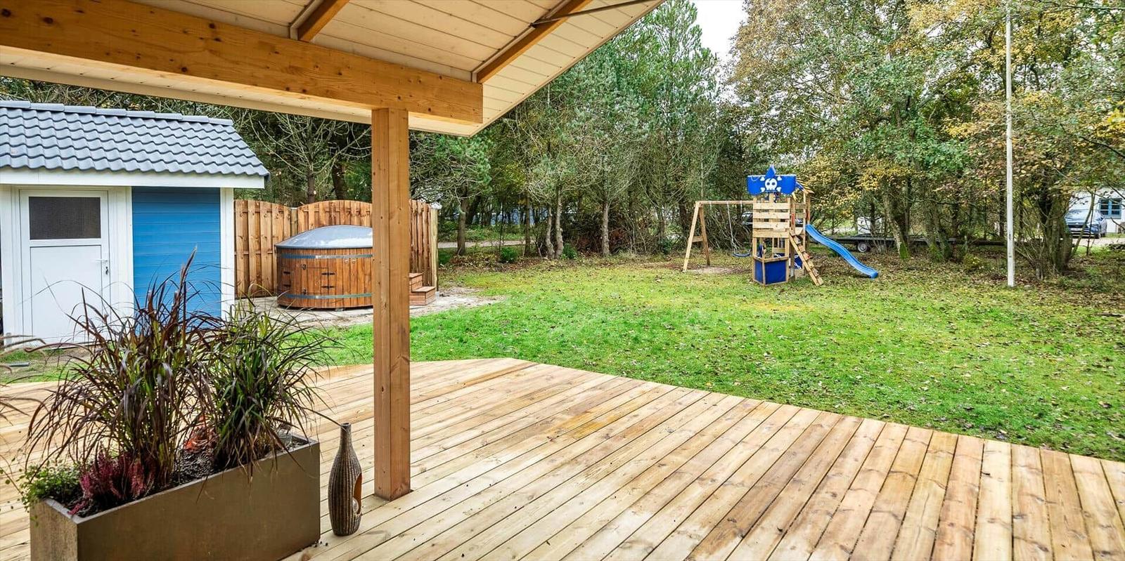 Holzterrasse mit Blick auf Garten, Spielplatz und Whirlpool.