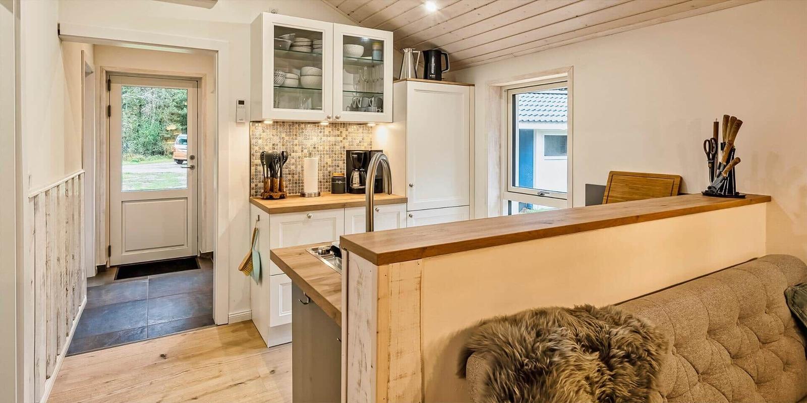 Küche mit Holzwerkzeugen und Glasvitrinen an der Wand. Eingangstür und Fenster sind sichtbar.