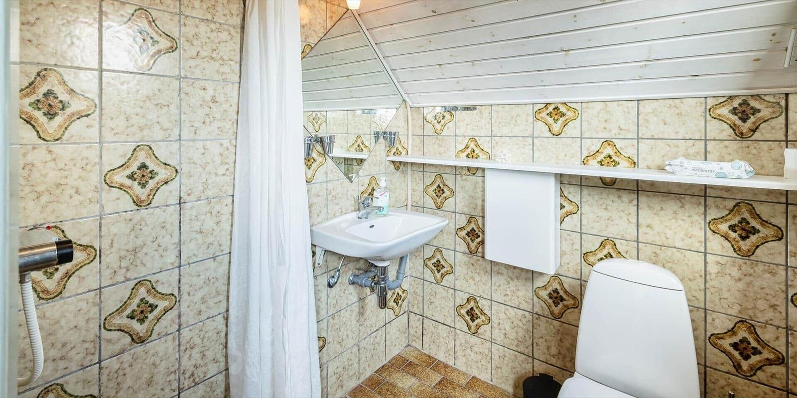 Badezimmer mit Duschvorhang, Waschbecken und Toilette. Wände mit gemusterten Fliesen.