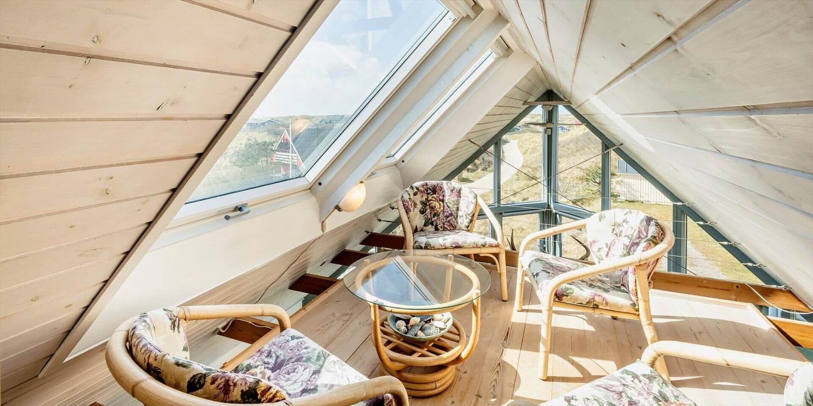 Dachgeschosszimmer mit Holzwand, Sitzgelegenheiten und großem Fensterblick.