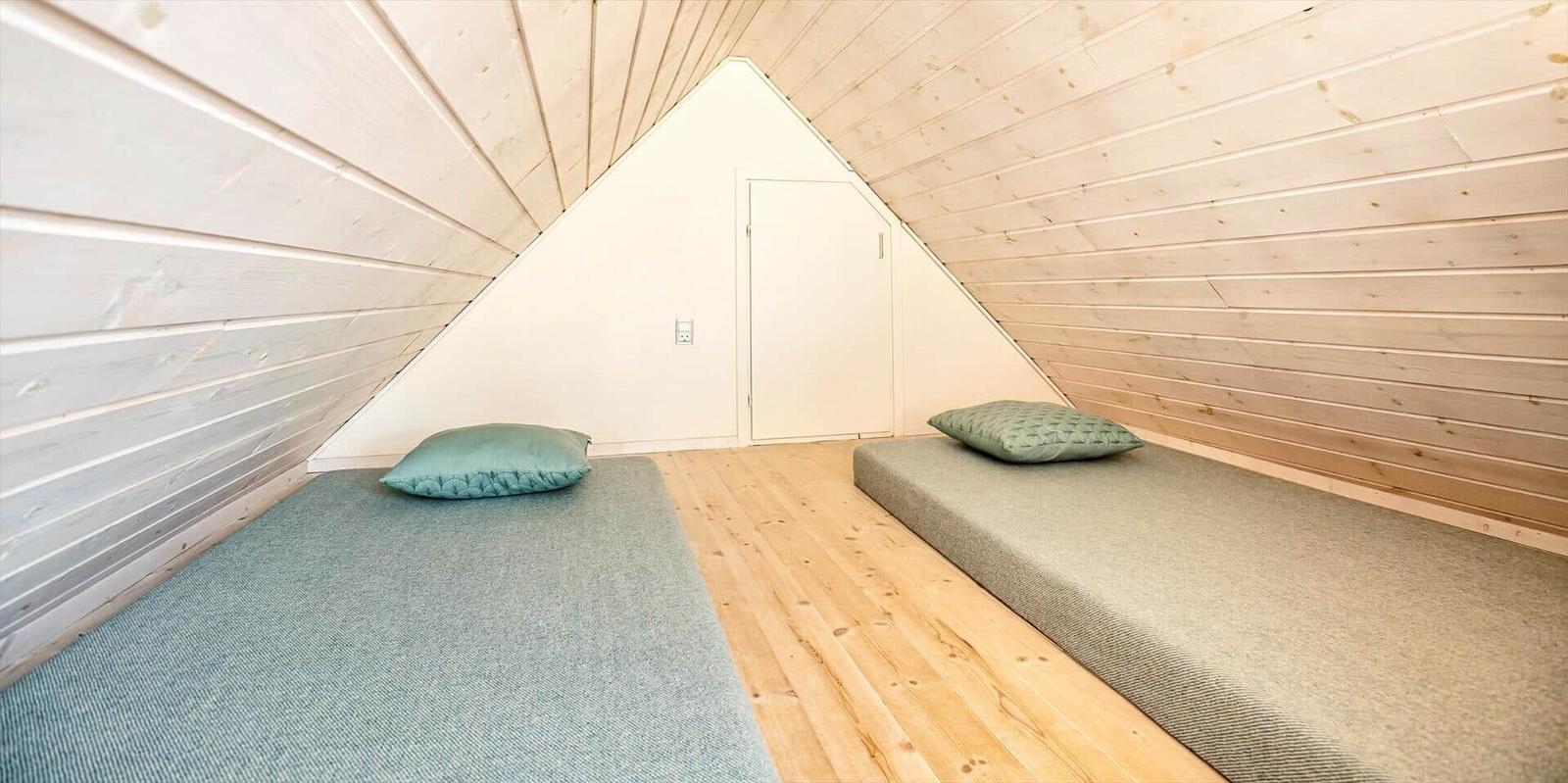 Zwei Schlafplätze in einem Dachbodenzimmer mit Holzwand und Boden.