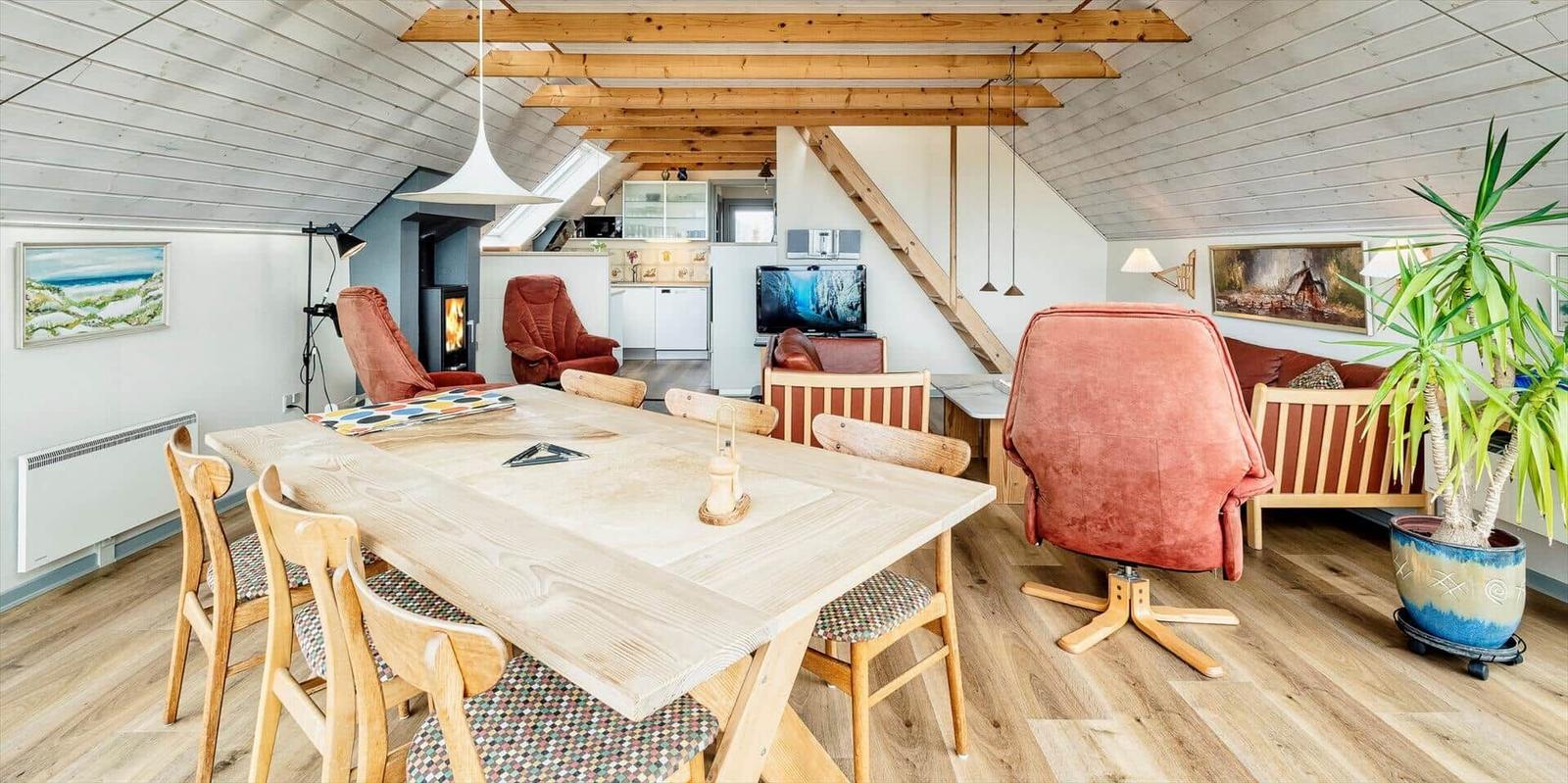 Eckzimmer mit Esstisch, Sesseln und Holzboden. Dachschrägen und Kamin sichtbar.