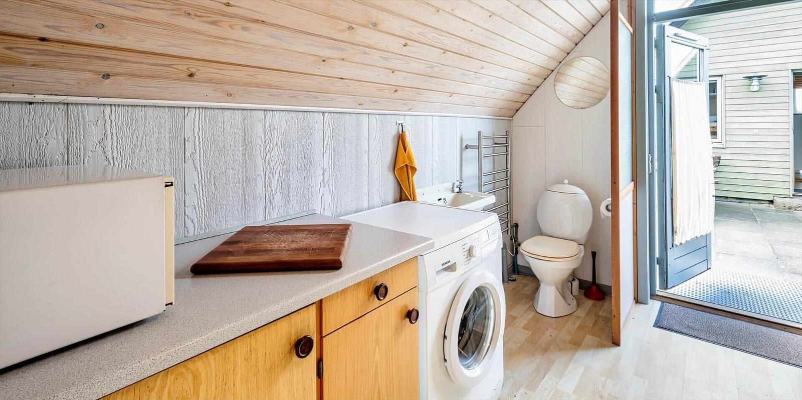 Wohnraum mit Waschmaschine, Spüle und Toilette. Holzdecke und -boden.