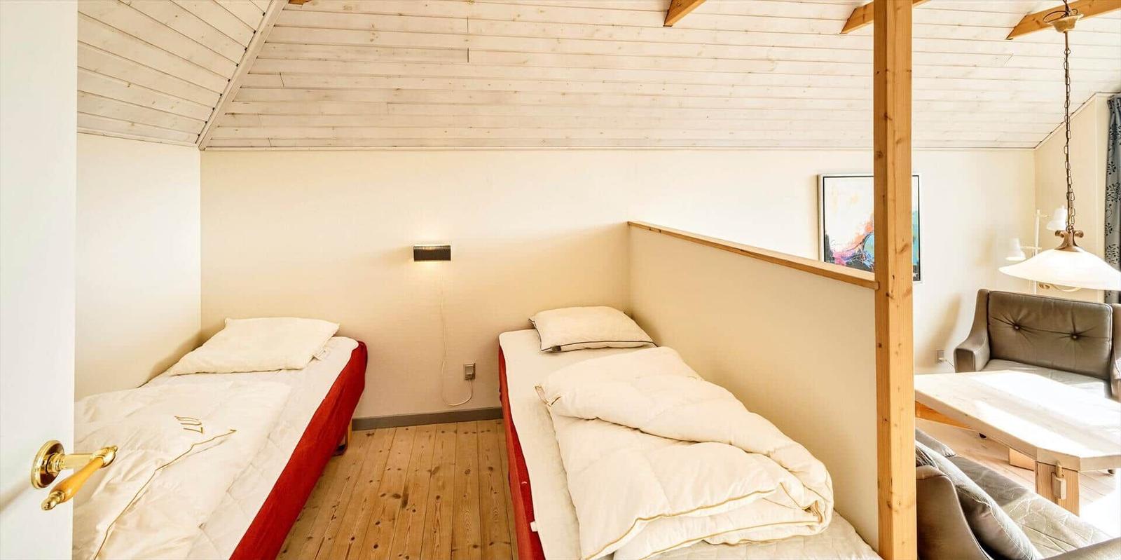 Zwei Einzelbetten in einem Raum mit Holzdecke und Boden. Im Hintergrund ist ein Sofa sichtbar.