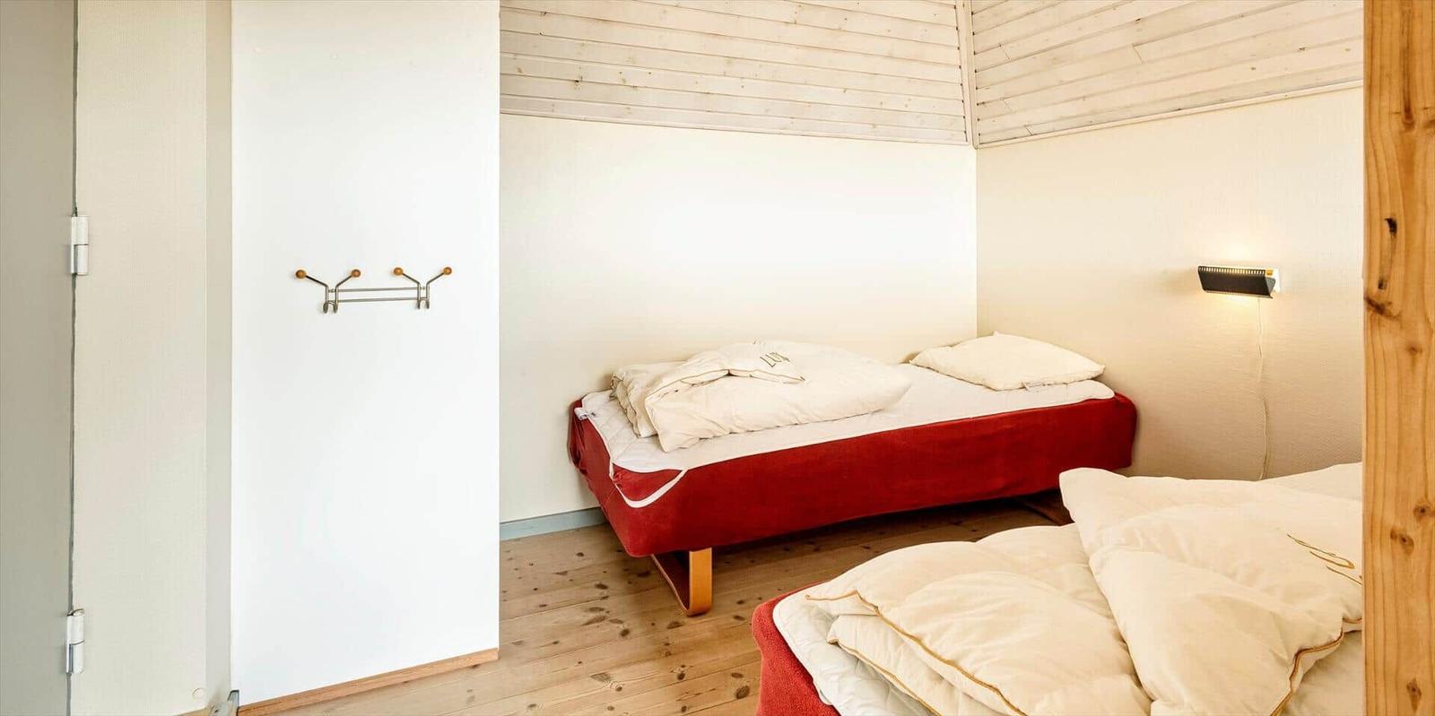 Zwei Betten mit weißen Bettwäsche in einem Raum mit Holzboden und weißen Wänden.