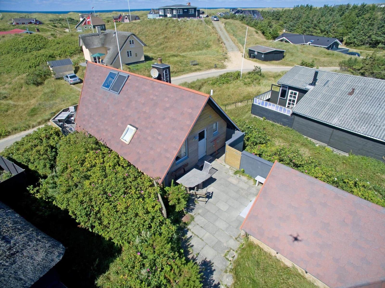 Haus mit Terrasse und Garten, umgeben von Grünflächen und weiteren Häusern.