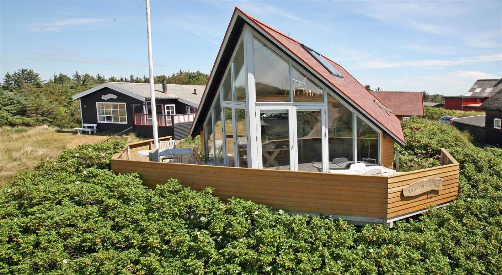 Moderne Holzhütte mit großem Glasbereich und Terrasse umgeben von Grünflächen.