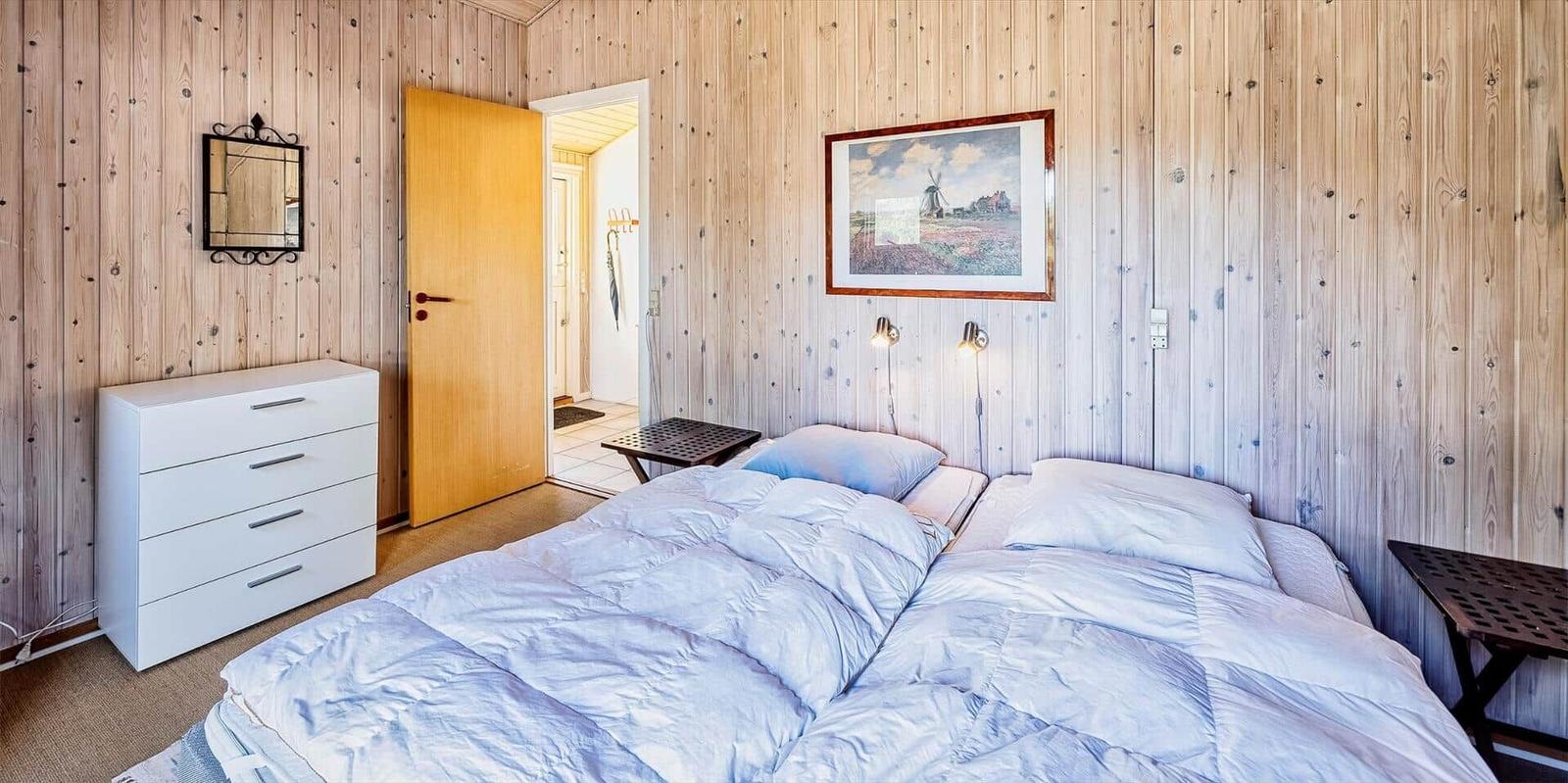 Schlafzimmer mit Holzwand, Bett, Schrank und Bild an der Wand.